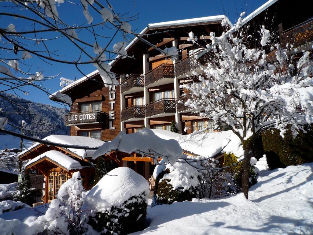 a snow covered building with a tree in front of it at Hôtel Les Côtes, Résidence Loisirs et Chalets in Morzine