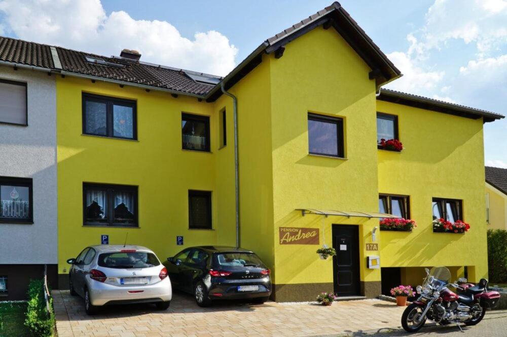 una casa amarilla con coches aparcados delante en Pension Andrea, en Lugau