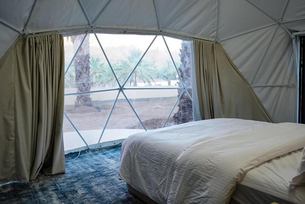 um quarto com uma cama numa tenda com uma grande janela em نيوم العلا em Al Ula