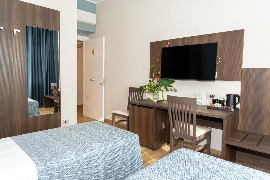 ein Hotelzimmer mit einem Bett und einem Schreibtisch mit einem Fernseher in der Unterkunft Lepanto Central in Messina