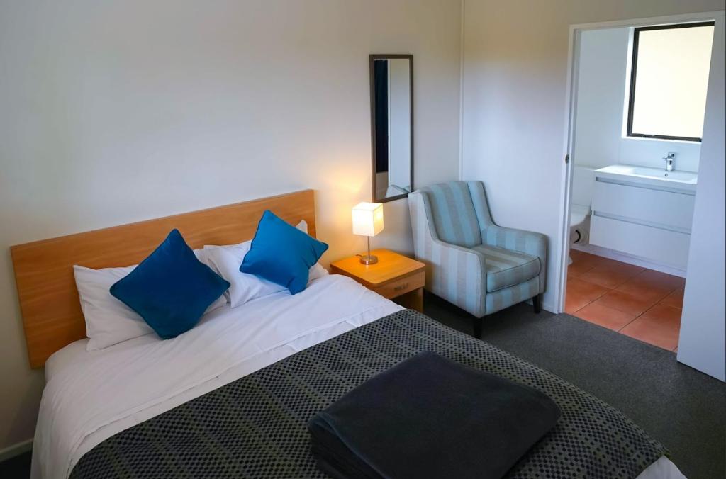 - une chambre avec un lit doté d'oreillers bleus et d'une chaise dans l'établissement Mt Aspiring Holiday Park, à Wanaka
