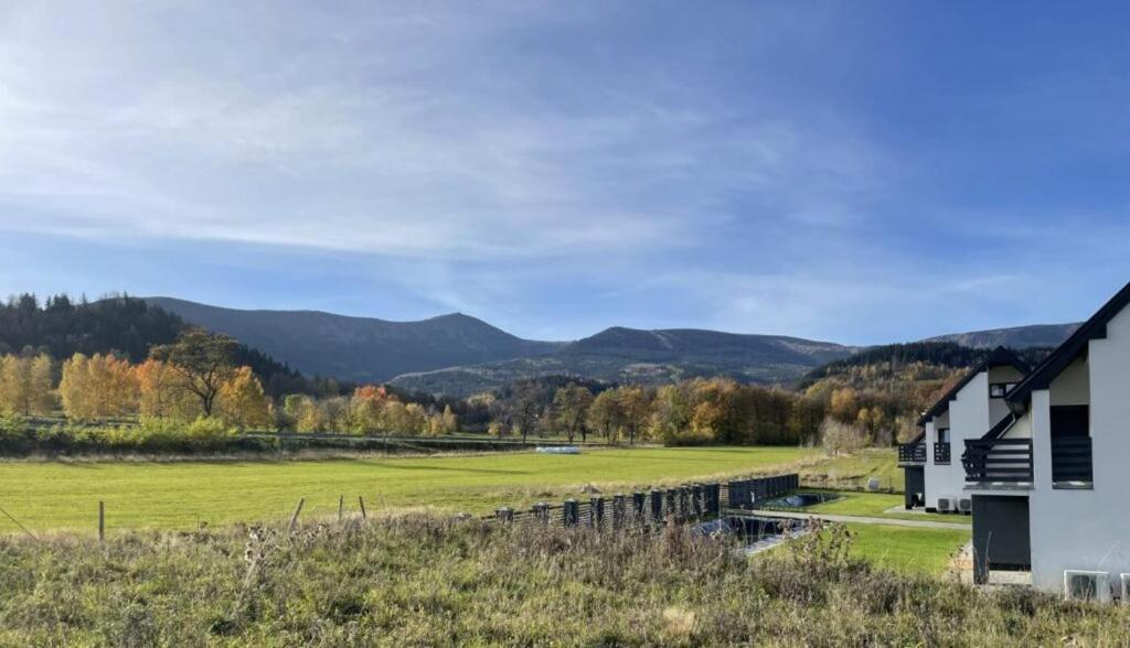 une maison et un champ avec des montagnes en arrière-plan dans l'établissement Top Escape - apartamenty z widokiem na góry - Przycup w Karkonoszach Apartamenty, à Karpacz