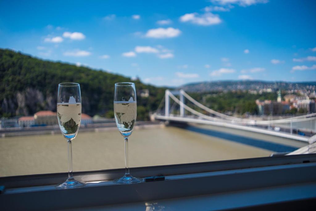 two wine glasses sitting on a window sill with a bridge at Flat with Unforgettable View in Budapest
