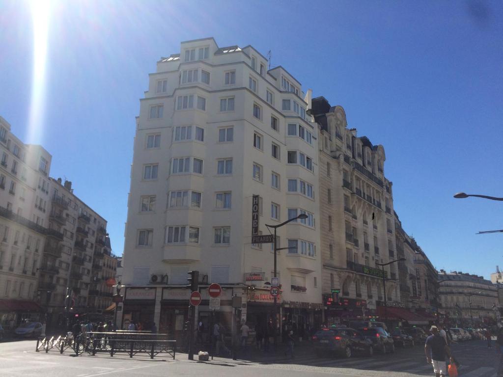 een hoog wit gebouw in een drukke stadsstraat bij Picardy Hôtel-Gare du Nord in Parijs