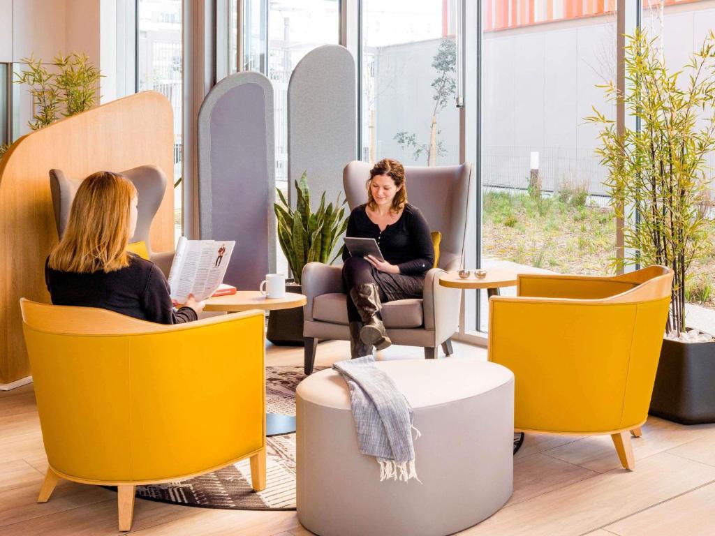 zwei Frauen sitzen auf Stühlen in einem Büro in der Unterkunft Aparthotel Adagio Access Paris Massy Gare in Massy