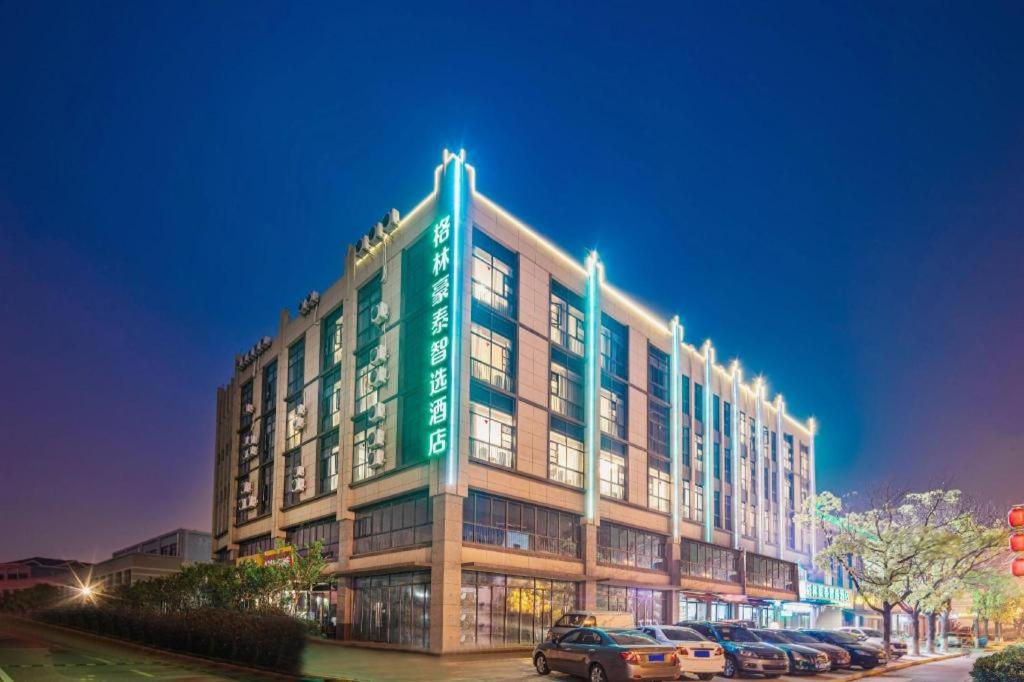 Un gran edificio con coches aparcados en un estacionamiento. en GreenTree Inn Express Zhangjiagang Hexing Town Shazhou Professional Institue of Technology, en Qiwei