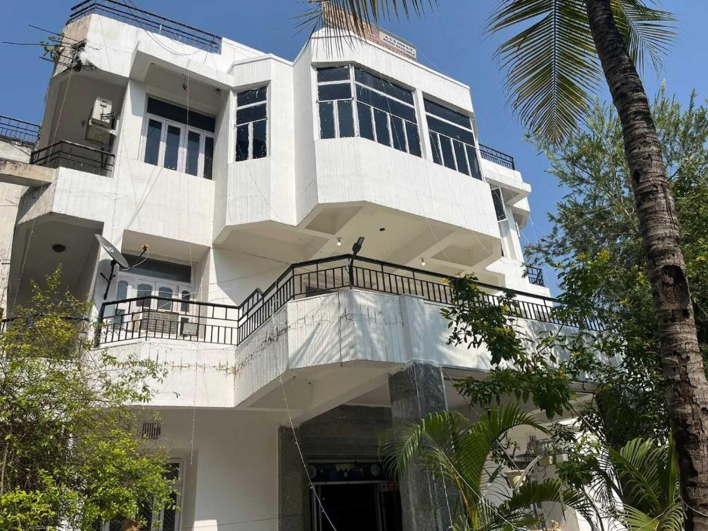 un bâtiment blanc avec un balcon et un palmier dans l'établissement Hotel O Buddha Statue Gaya Formerly Uruvela International, à Bodh Gaya