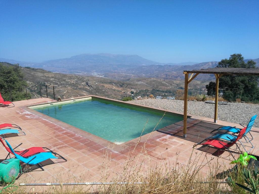 a swimming pool with two chairs and a umbrella at Casitas El Paraje de Berchules in Bérchules