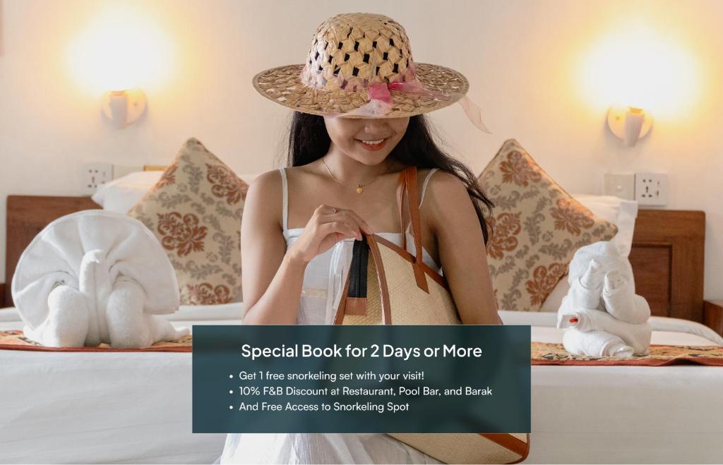 a woman wearing a straw hat sitting on a bed at Amed Cafe & Hotel Kebun Wayan in Amed