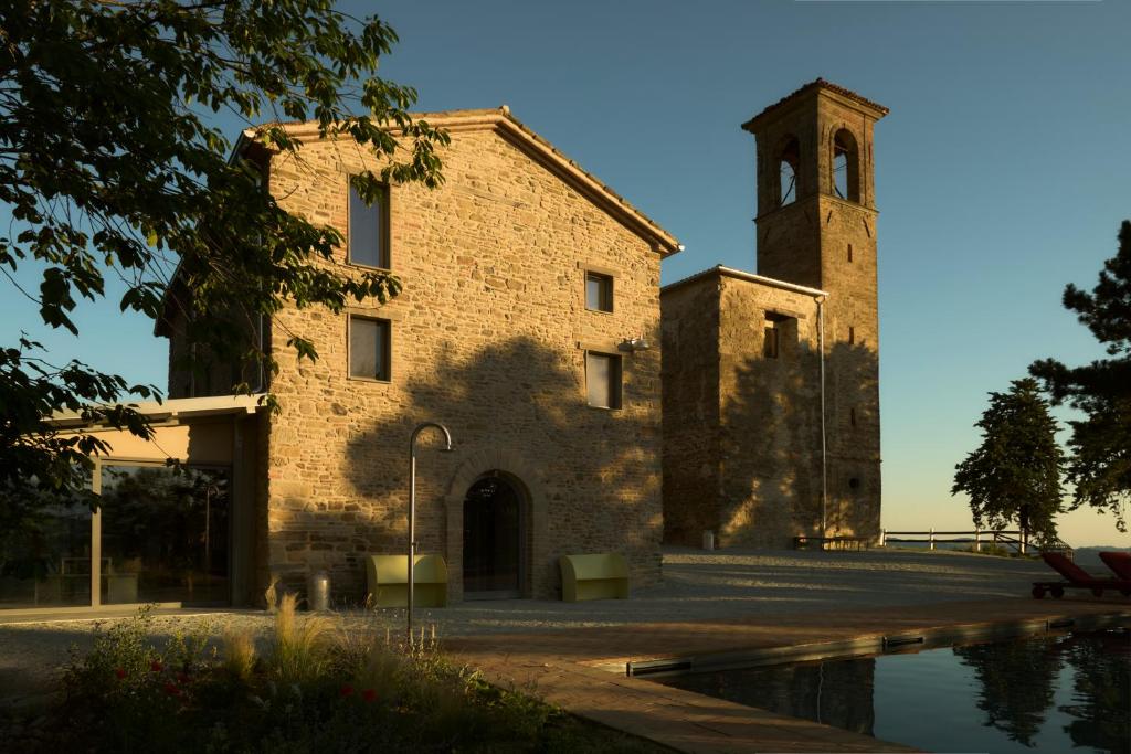 Ein großes Steingebäude mit einem Uhrturm neben einem Pool in der Unterkunft Scavolo Borgo in SantʼAgata Feltria