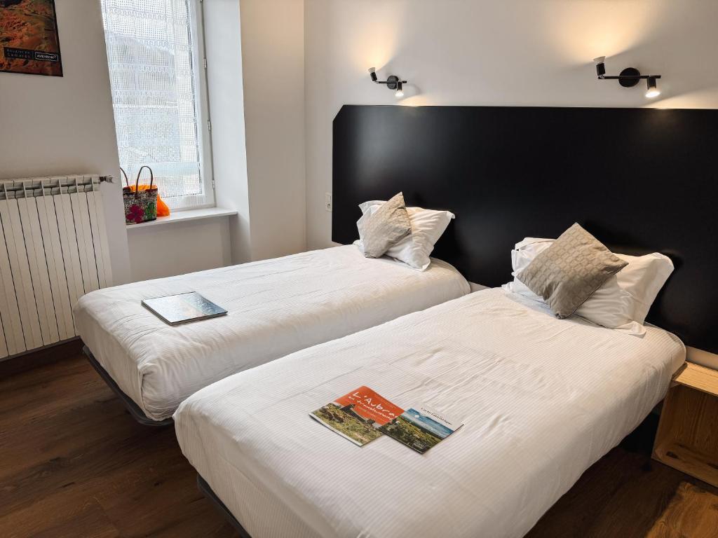 2 Betten in einem Zimmer mit 2 Büchern drauf in der Unterkunft Hôtel des Voyageurs in Saint-Chély-dʼAubrac