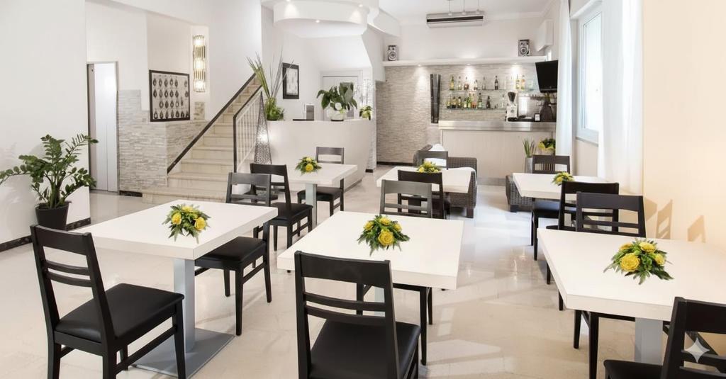 ein Restaurant mit weißen Tischen und schwarzen Stühlen in der Unterkunft Hotel Ferrara in Cattolica