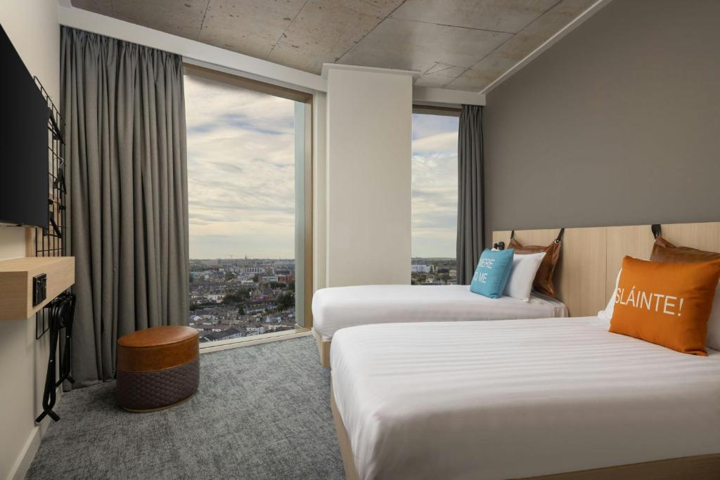 a hotel room with two beds and a large window at Moxy Dublin Docklands in Dublin