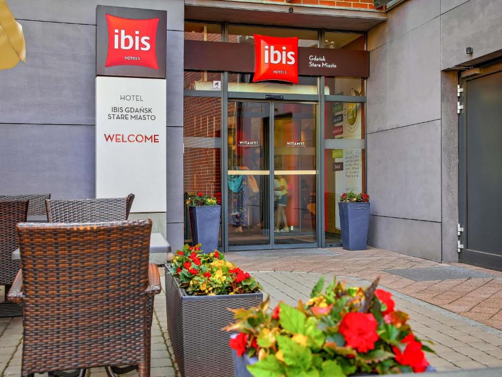 une table avec des fleurs et des chaises devant un magasin dans l'établissement Ibis Gdansk Stare Miasto, à Gdańsk