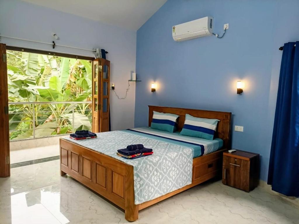 a bedroom with a bed with blue walls and a window at Roque's Place Goa in Betalbatim