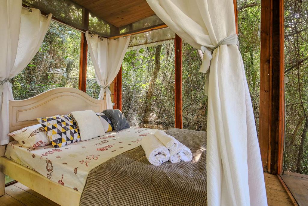 ein Schlafzimmer mit einem Bett in einem Zimmer mit Fenstern in der Unterkunft Casa de Vidro na Mata há 90km de São Paulo, com Lago, Piscina, Caiaque, Stand UP, Cascata e Escorrega no Lago - Quinta do Vale Itatiba in Itatiba