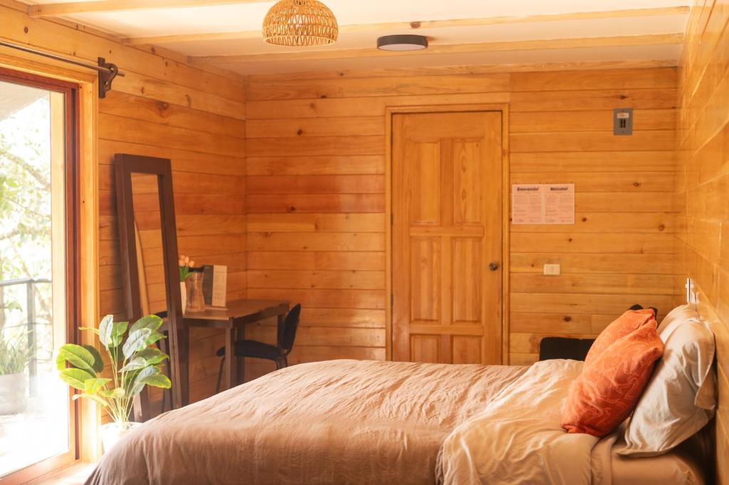Schlafzimmer mit Holzwänden, einem Bett und einem Fenster in der Unterkunft San José del Pacífico- Cabañas Camino al Cielo 2 in San Mateo Río Hondo