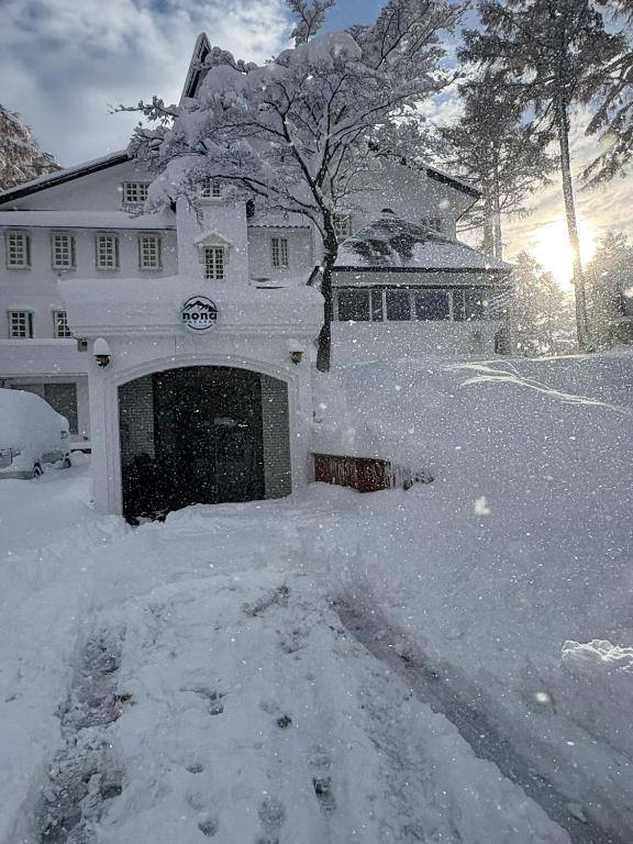 a snow covered house with a garage in front of it at Nona Madarao in Madarao Kogen