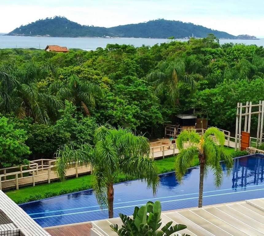 a view of a swimming pool with trees and water at Refúgio VIP Pé na Areia no Campeche - Piscina, Sauna e Academia até 08 pessoas in Florianópolis