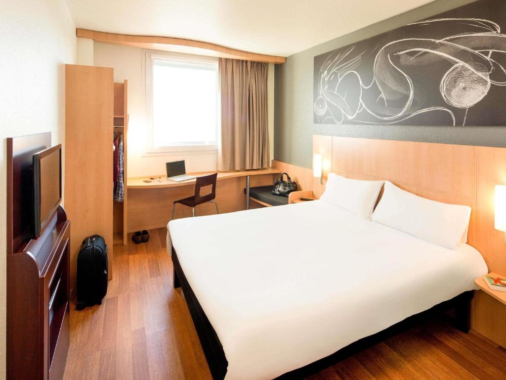 a hotel room with a large bed and a desk at Ibis Barcelona Meridiana in Barcelona