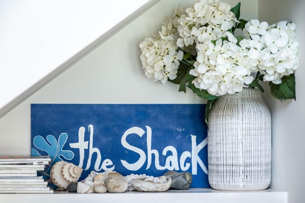 Eine Vase mit weißen Blumen und ein Schild auf einem Regal in der Unterkunft The Shack in Seal Rocks