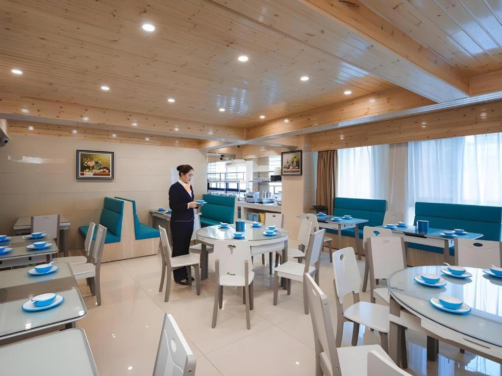 a woman standing in a restaurant with tables and chairs at Vienna Hotel Shandong Liaocheng High-Tech Zong Yueji Park in Liaocheng