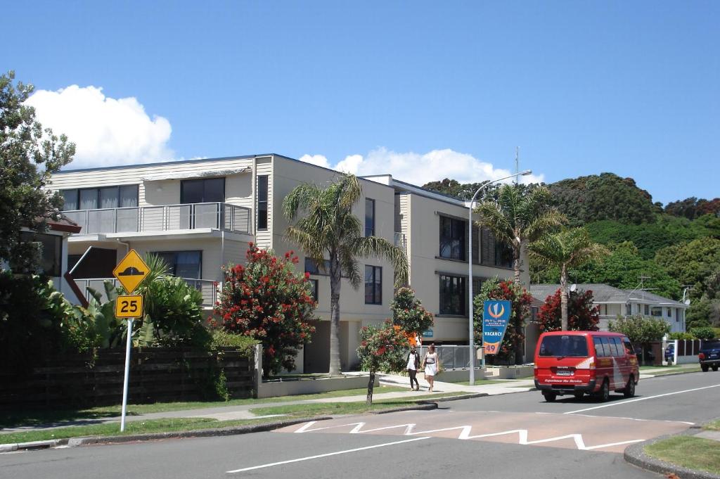 una furgoneta roja conduciendo por una calle al lado de un edificio en Atlas Suites and Apartments, en Mount Maunganui