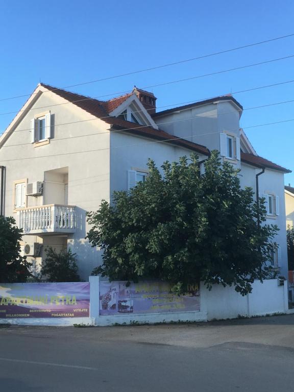 une maison blanche avec un arbre devant dans l'établissement Apartments Petra, à Biograd na Moru