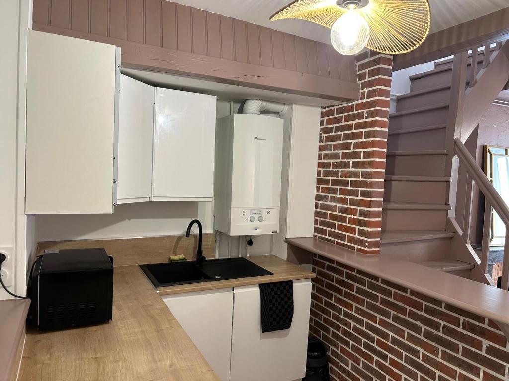 a kitchen with white cabinets and a brick wall at jolie maison de ville proche bords de Loire in Châteauneuf-sur-Loire