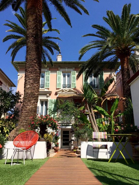une chaise rouge assise devant une maison plantée de palmiers dans l'établissement Hotel Villa Rose, à Nice