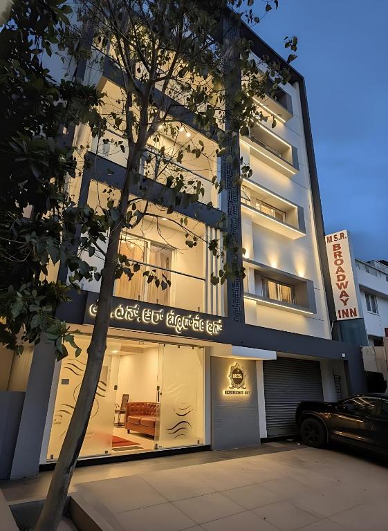 a building with a tree in front of it at Broadway Inn in Mysore