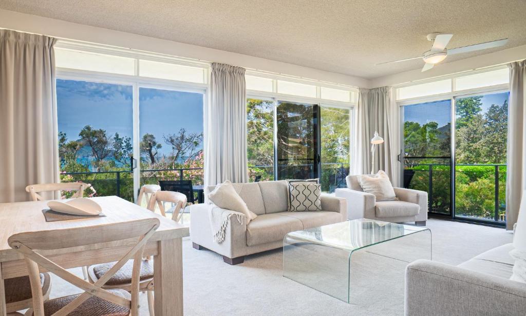 Una sala de estar con muebles blancos y grandes ventanales. en The Helm Unit 1 22 Voyager Close, en Nelson Bay
