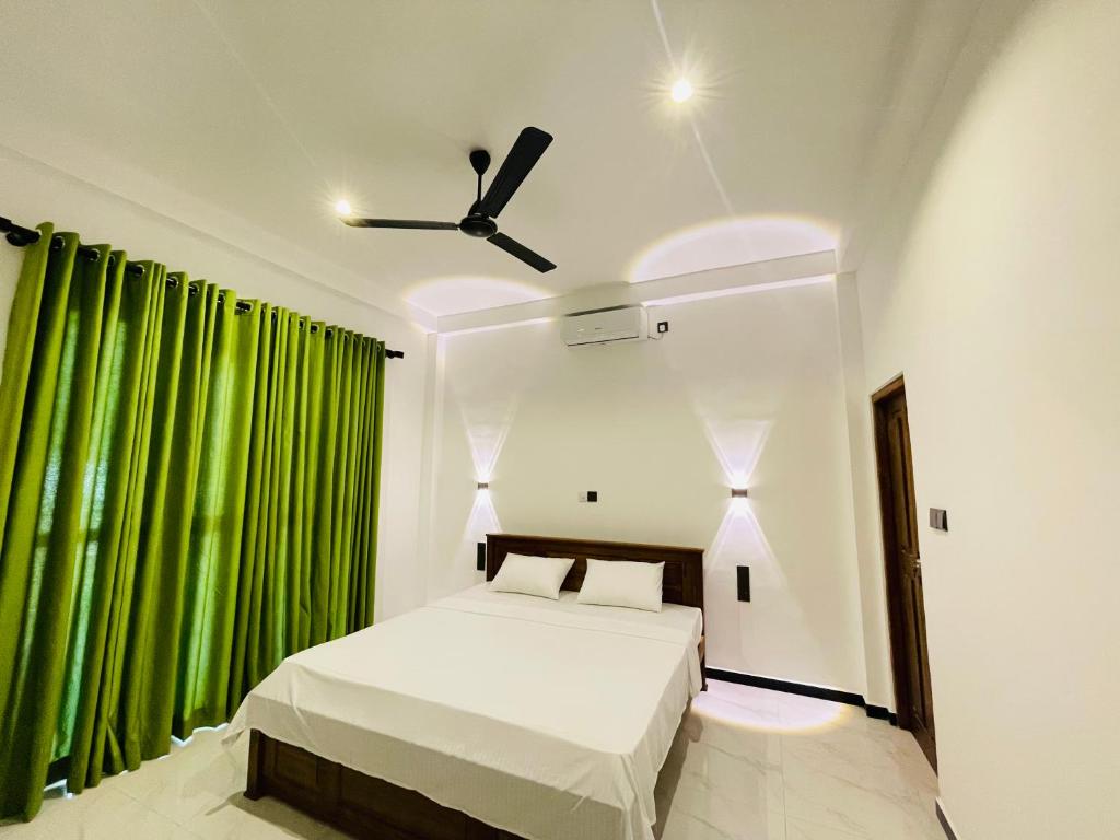 Schlafzimmer mit einem Bett mit grünen Vorhängen und einem Deckenventilator in der Unterkunft THE PRASINOS villa & resort in Habaraduwa Central