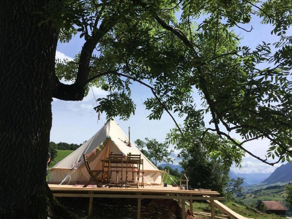 une tente en toile avec une terrasse et un arbre dans l'établissement Zeltferien Into The Wäid Zelt Unter Der Esche, à Ennetmoos