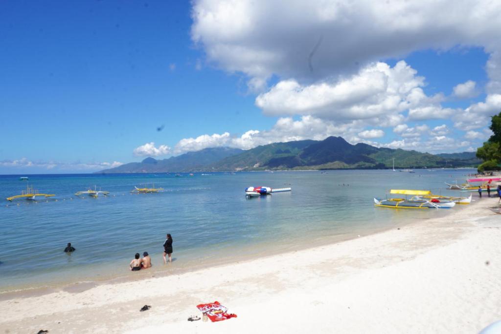 Les gens sur une plage avec des bateaux dans l'eau dans l'établissement Palazio De Laiya Resort Hotel, à San Juan