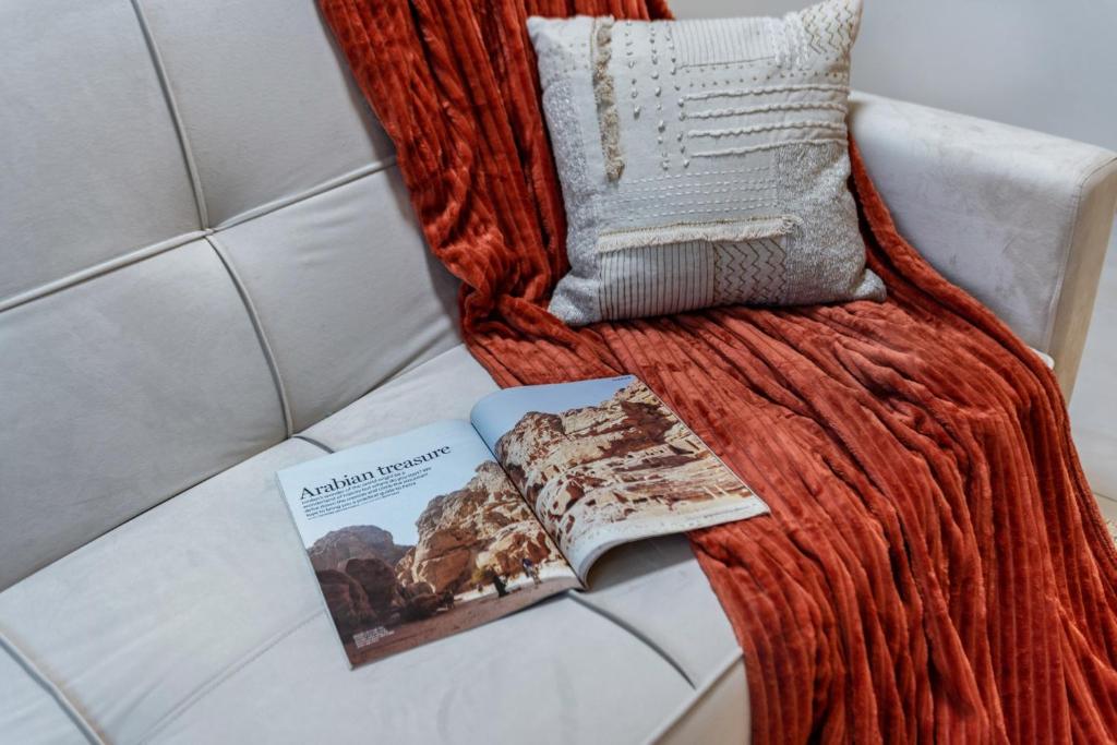 a book and a pillow on a couch with a book at The Living khorfakan Cornish 2 in Khor Fakkan