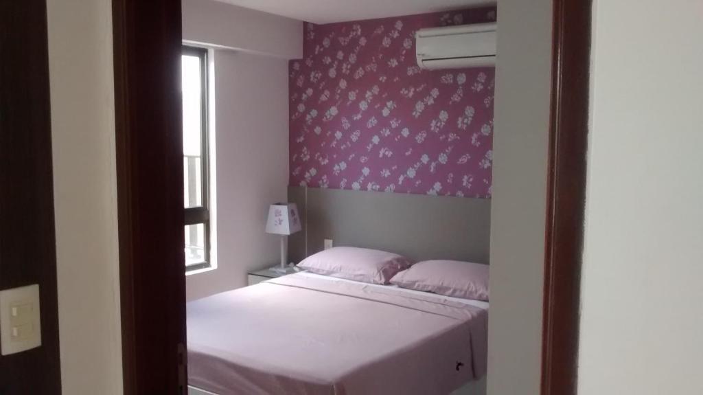 Dormitorio pequeño con cama y pared de color rosa en Lindo Apartamento à Beira Mar, en João Pessoa