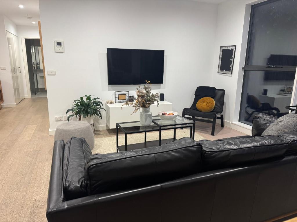 ein Wohnzimmer mit einem schwarzen Ledersofa und einem TV in der Unterkunft Beautiful light filled modern apartment in Kew in Melbourne