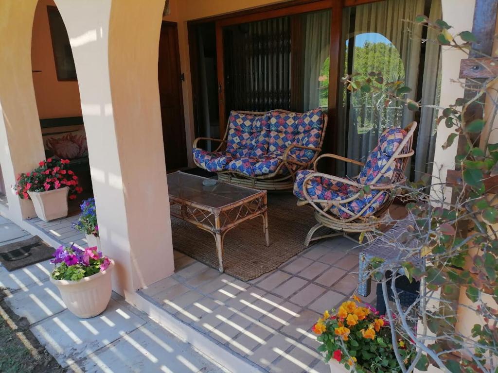 a porch with two chairs and a table and flowers at Coral Tree SelfCatering in St Francis Bay
