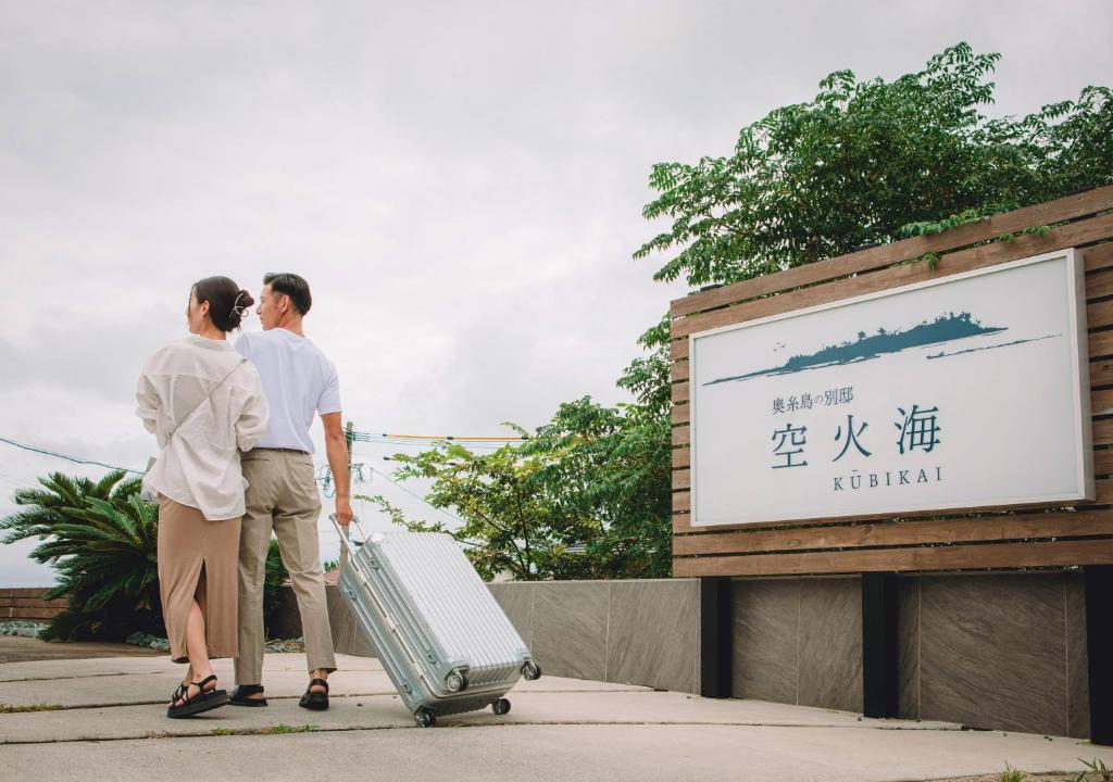 two people standing in front of a sign with a suitcase at Kubikai in Itoshima