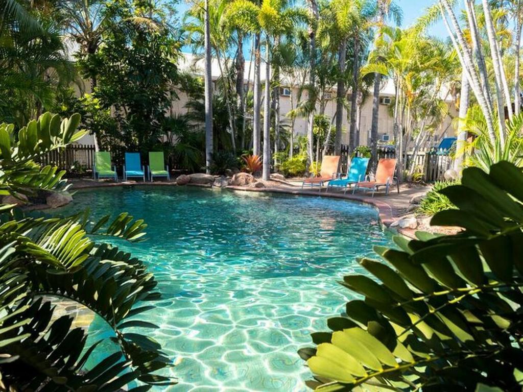 a swimming pool with blue chairs and palm trees at The Beach Motel Hervey Bay in Hervey Bay