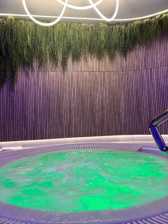 Circular whirlpool with green-lit bubbling water, vertical wooden slat wall and hanging greenery.