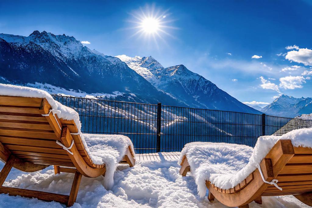 um pátio coberto de neve com dois bancos e montanhas em Mattertal Lodge em Embd