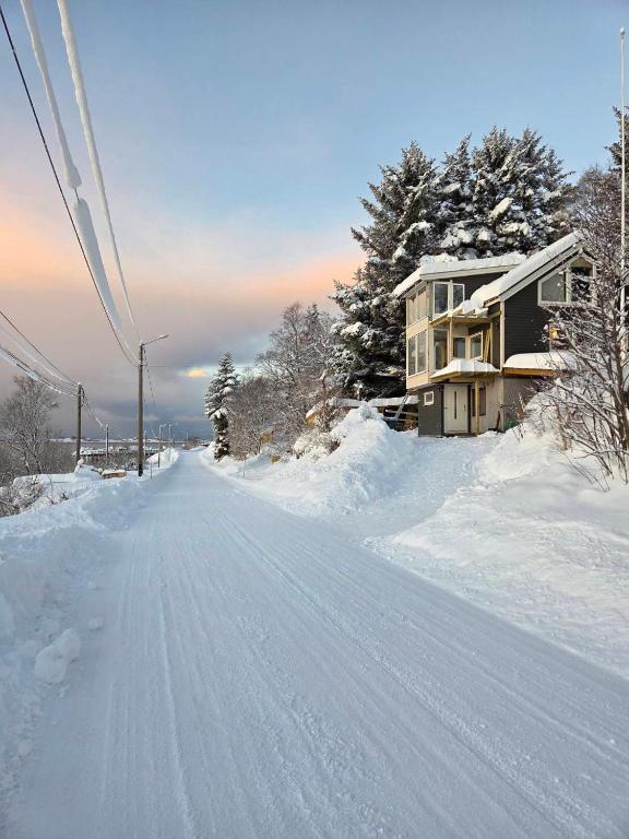 a street covered in snow with a house in the background at Senja, Skaland apartment in Skaland
