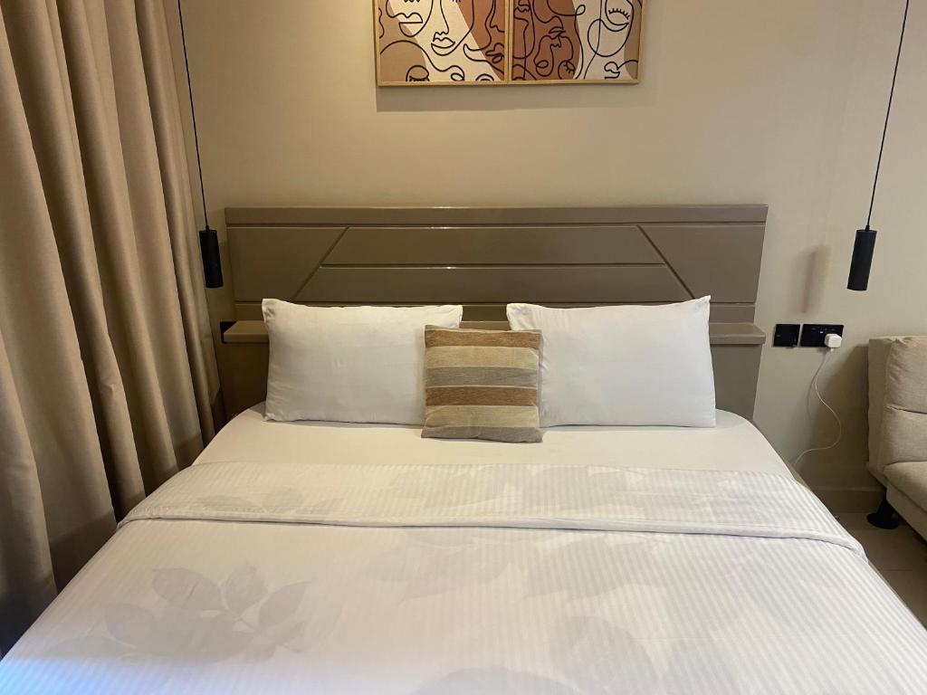 un lit avec des draps blancs et des oreillers dans une chambre dans l'établissement Belrose Place Studio Apartment, à Accra