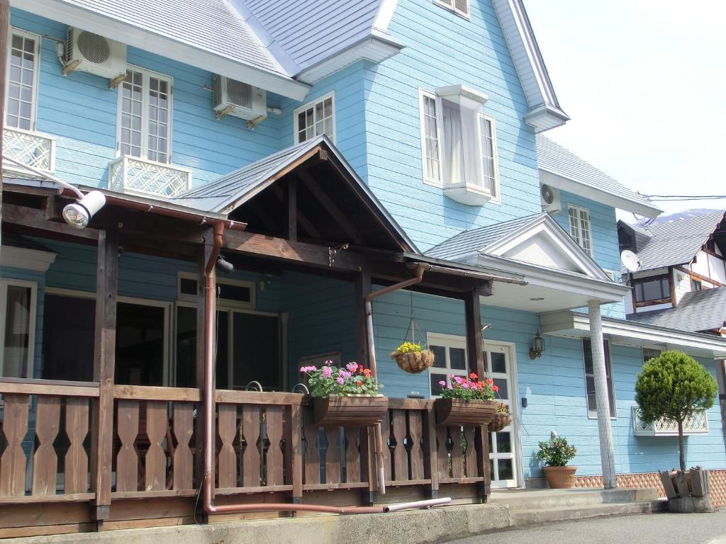 une maison bleue avec une véranda fleurie dans l'établissement Pension Come, à Minami Uonuma