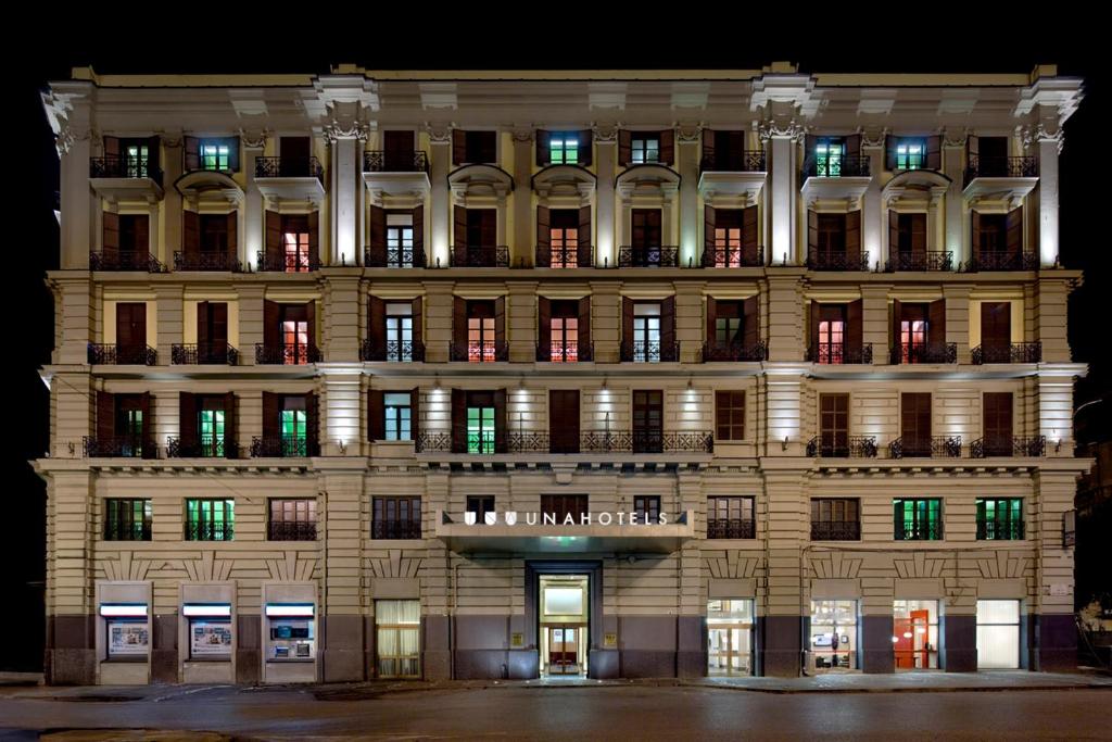 um grande edifício com janelas iluminadas à noite em UNA Hotels Napoli em Nápoles