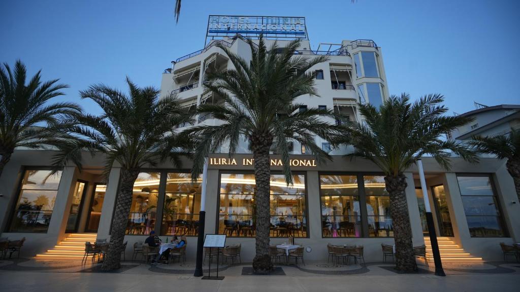 a building with palm trees in front of it at Iliria Internacional Hotel in Durrës