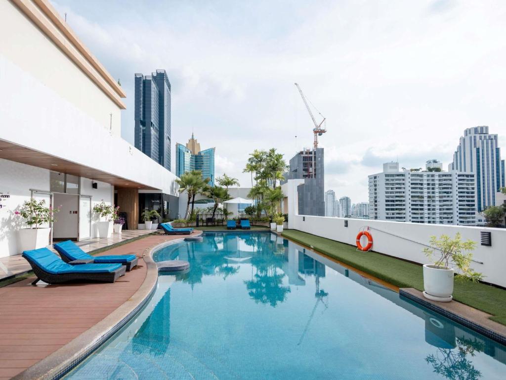 uma piscina com cadeiras azuis e edifícios em Grand Mercure Bangkok Asoke Residence em Banguecoque