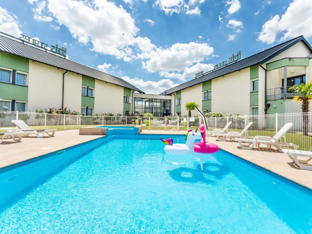 a swimming pool with a pink inflatable toy in front of a building at Hôtel Ibis Styles Bourges - Piscine extérieure chauffée - Restaurants à proximité in Bourges